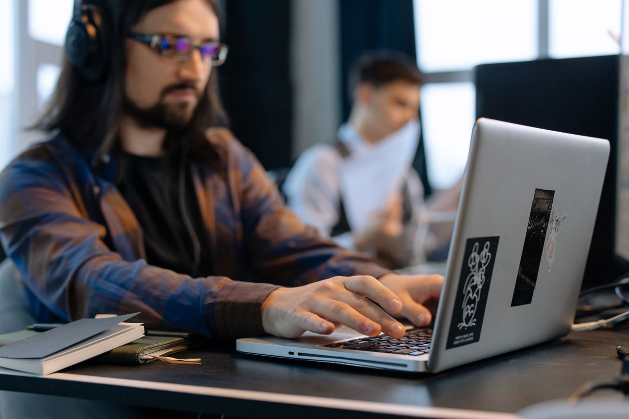 team-04 A man wearing headphones focused on typing at his laptop in a contemporary office setting.